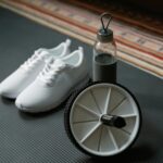 A close-up of white sneakers, ab roller, and water bottle on a yoga mat, ideal for fitness routines.