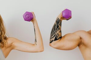 Two individuals flexing their muscles with fixed dumbbels.